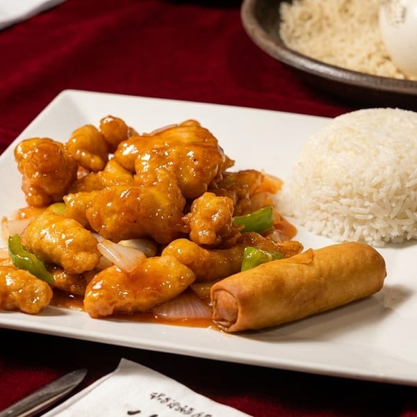 Sweet and sour chicken with white rice and an egg roll on a white plate.